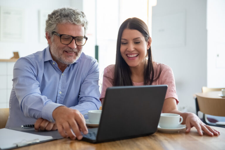 Happy cheerful mature man and young woman sitting at laptop