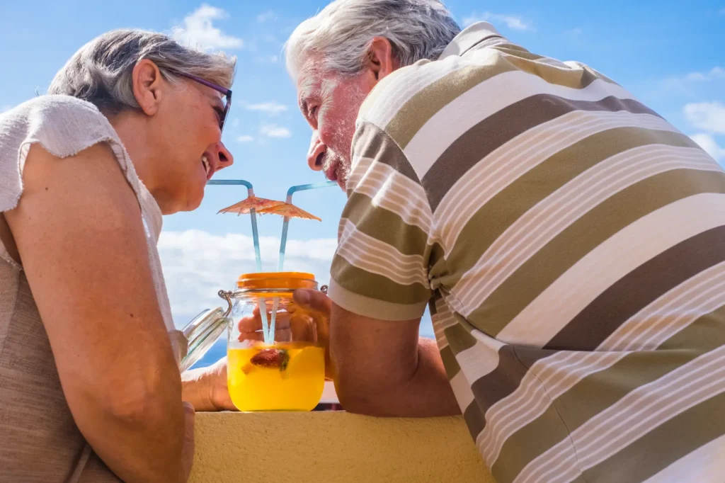 Senior couple drinking cocktail retaining wall against sky
