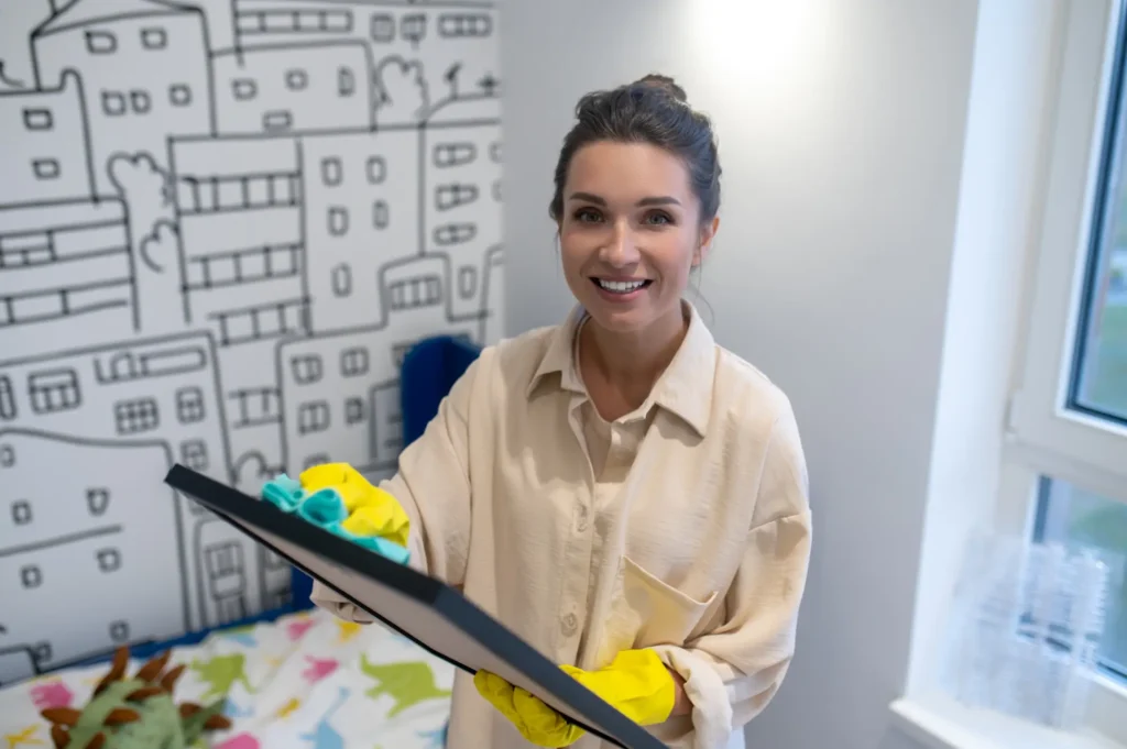Waist up portrait smiling cleaning lady latex gloves wiping dust off photo frame with microfiber cloth